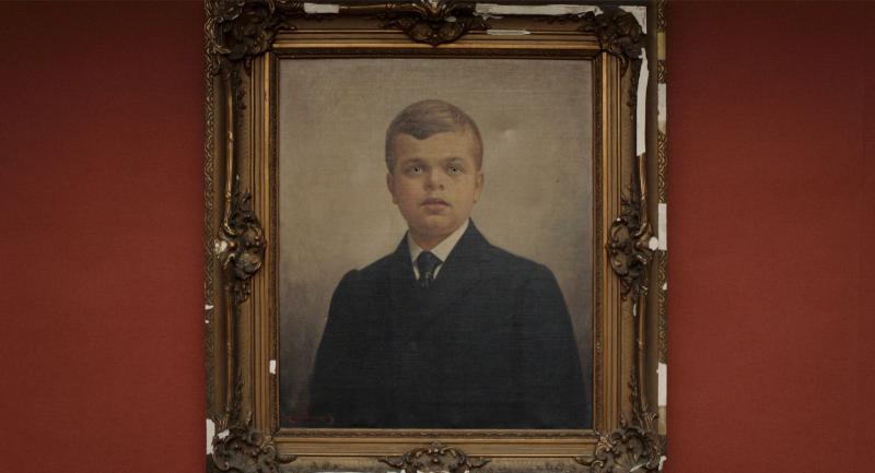A framed painting of a young white boy on a red wall.