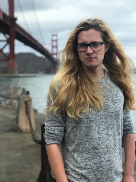 Max in front of Golden Gate Bridge, he has long blond hair and glasses.