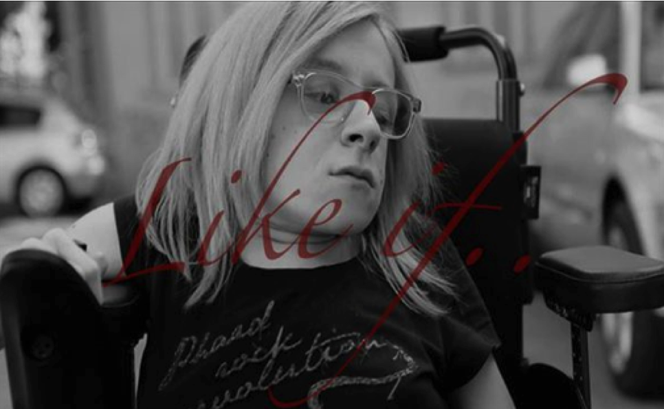 A black and white photograph of a blond woman wearing glasses sitting in a wheel chair stares off into the right corner of the frame.