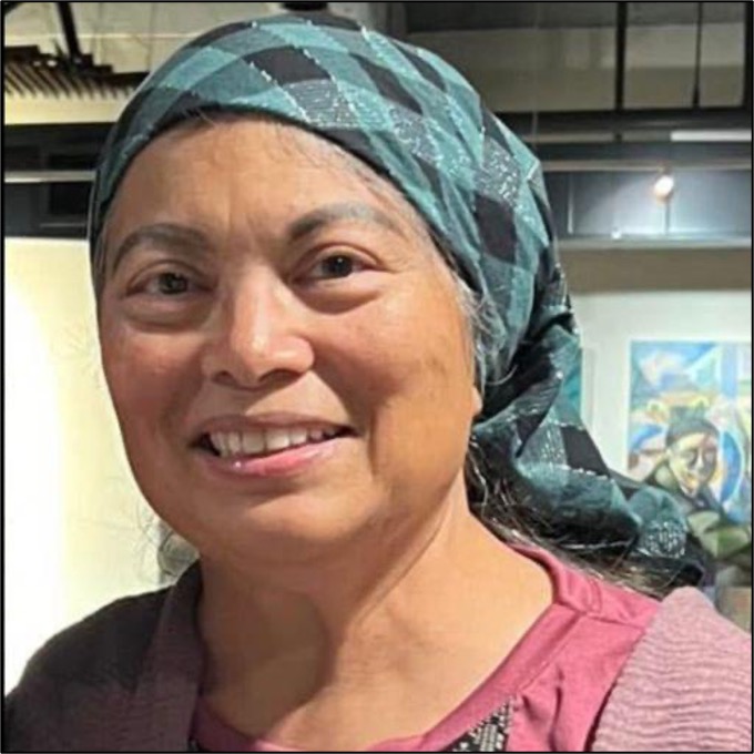 Titania, an Alaskan and Ilocano/Ibanag person with brown skin smiling into the camera. She wears a light blue and navy blue checkered head scarf and a pink top.