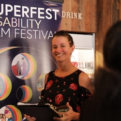 Emily Beitiks, a white woman with brown hair pulled back, wears a floral shirt in front of a Superfest sign.